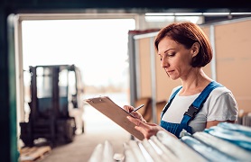 Woman checking inventory using clipboard in an industrial setting.