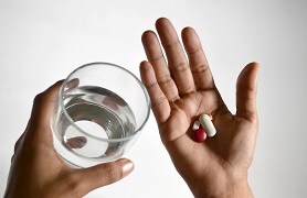 hand holding glass of water, another holding pills